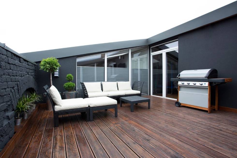 Grill and white garden furniture on wooden floor of terrace